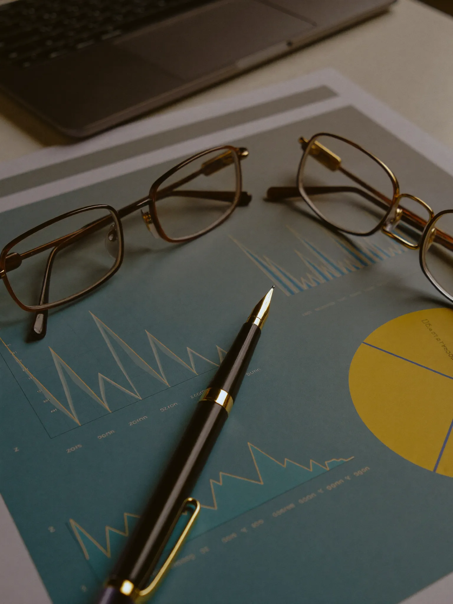A business strategy report with charts on a desk, a fountain pen and a pair of glasses resting on it